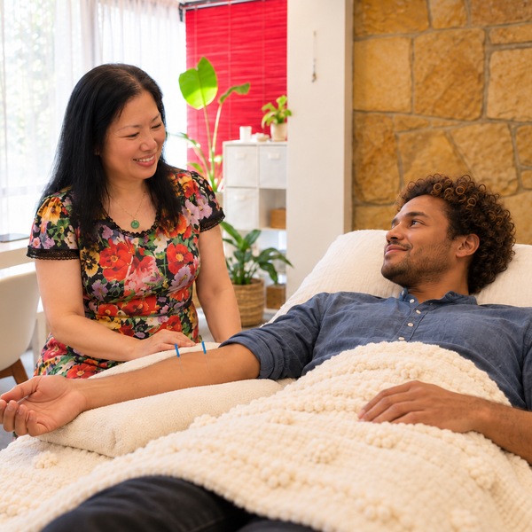 Illustrative, Freshwater: Dr Christine Shen, Acupuncturist, in a floral top, sits by a patient with curly hair resting with needles in his forearm.