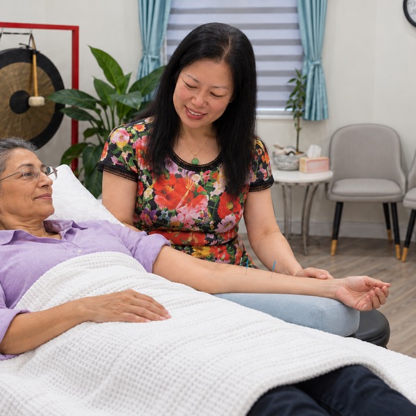 Illustrative, Lane Cove: Dr Christine Shen, Acupuncturist, supports the outstretched arm of a patient in a lilac shirt lying on a treatment table.